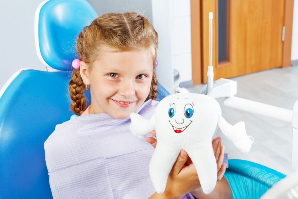 cheerful child in dentist seat holding a toy tooth
