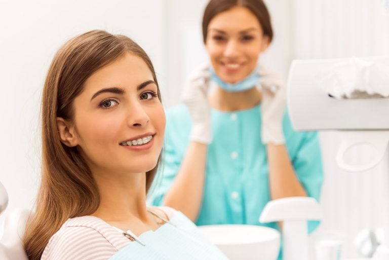 orthodontics portrait of a happy patient with braces on the teeth, sitting in the dental chair, in the background a young doctor dentist