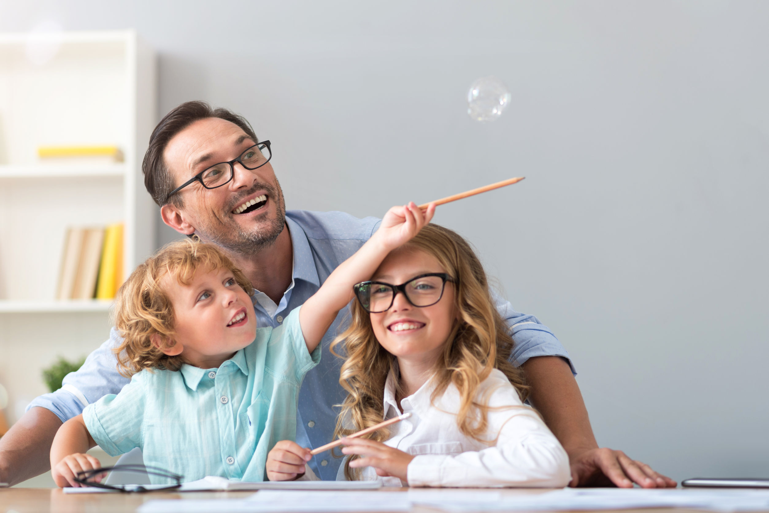 lift it higher. joyful little boy trying to catch a soap bubble with a pencil while sitting at the table with a smiling man and adorable girl