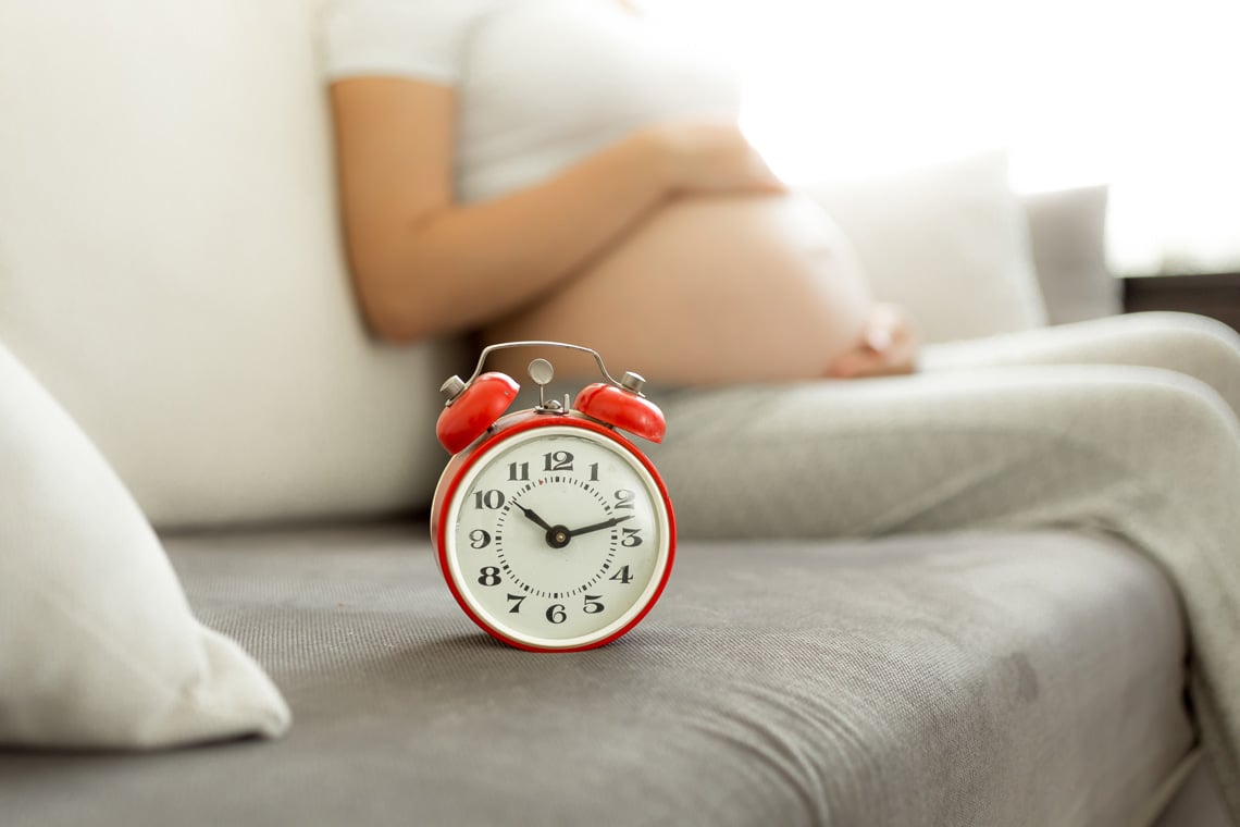 Waiting-for-baby.-Alarm-clock-against-pregnant-woman