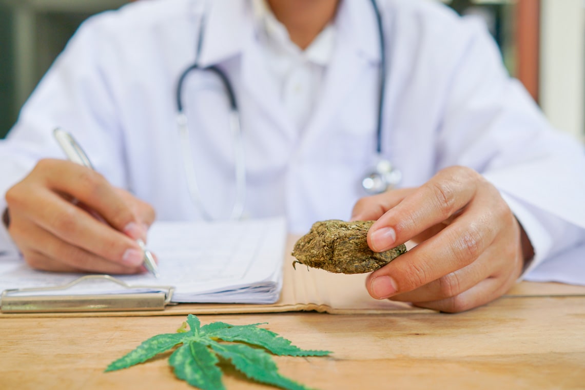 doctor-writing-on-prescription-blank-and-bottle-with-medical-cannabis-on-table-close-up