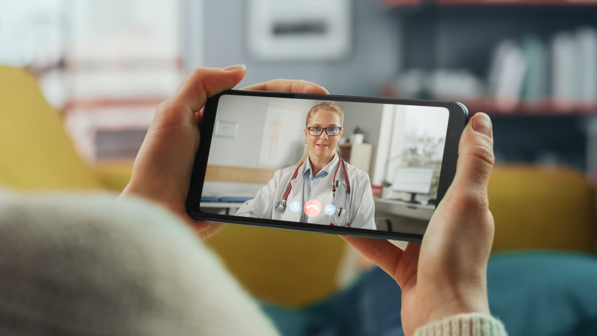 Special Benefits Insurance Services | Growing Your Small Business? GMS Group Advantage Health Grows With You Close-up of hands holding a smartphone displaying a video call with a smiling female doctor wearing a lab coat and stethoscope.