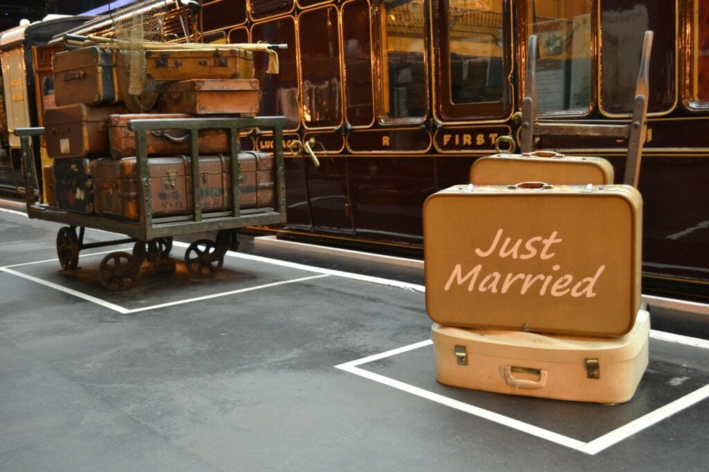 Stacks of luggage in front of a train car, with the text "Just Married", preparing for a "buddymoon" vacation
