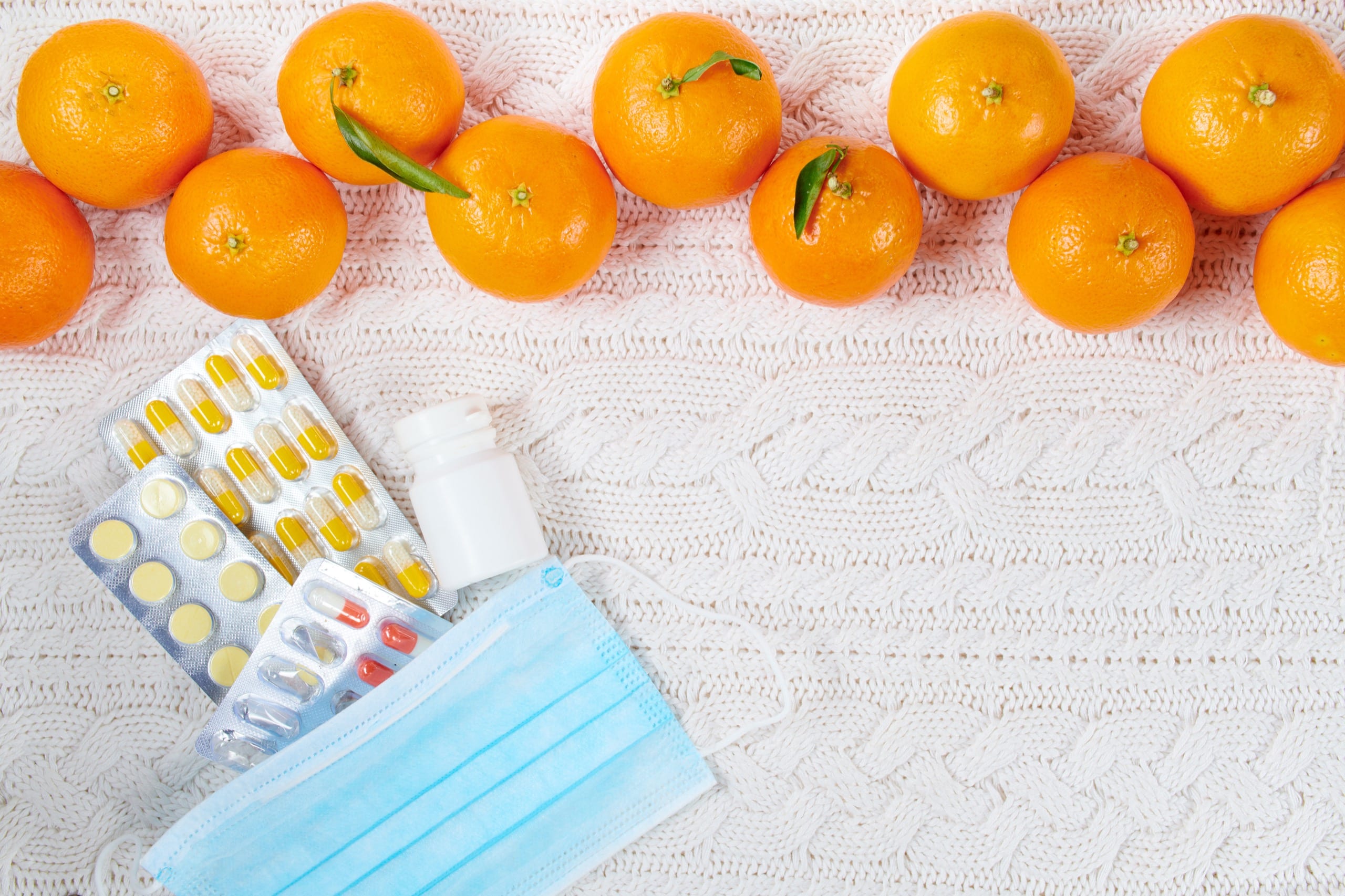 Special Benefits Insurance Services | How Health Insurance Can Help You Stay Healthy This Fall Winter flat lay with medical mask, pills and mandarins on white knitted background.