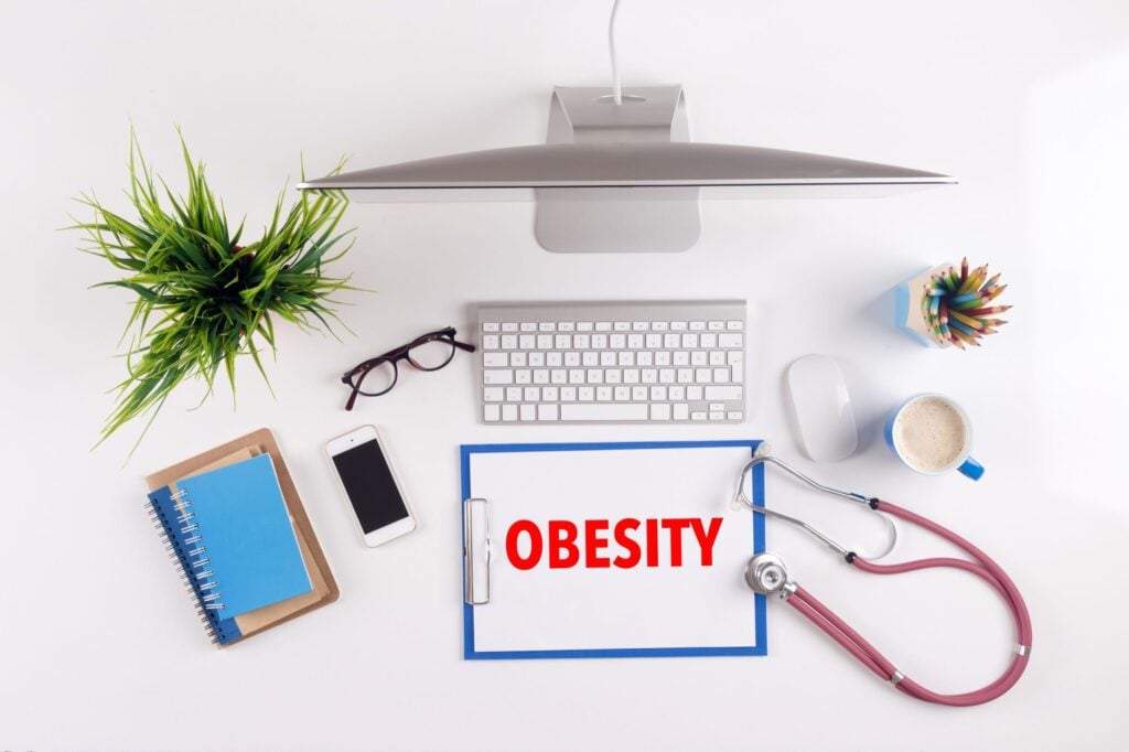 "Obesity" written on a clipboard, surrounded by desk accessories and a stethoscope