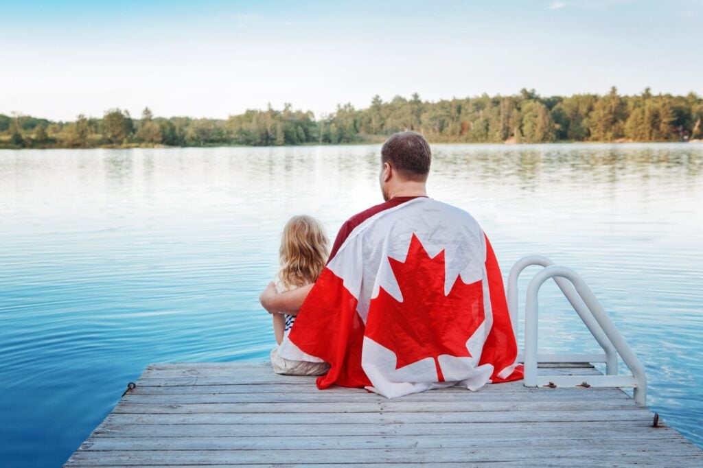Father and daughter sitting on a dock draped in a Canadian flag