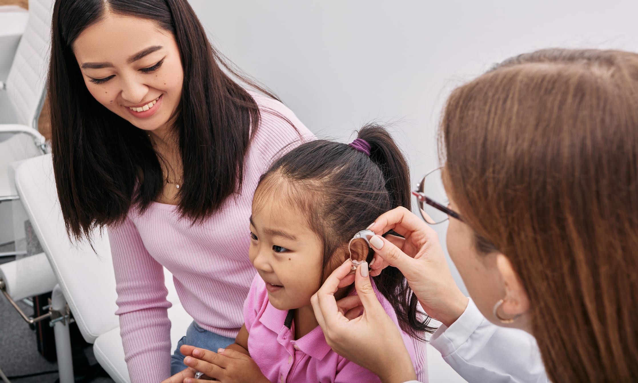 Small child being fitted for a hearing aid while her mom smiles