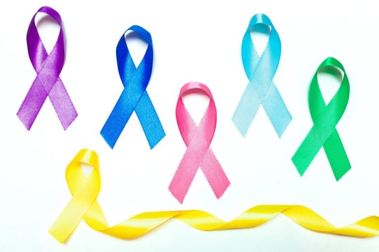 A collection of colorful awareness ribbons, including purple, blue, pink, and green, arranged on a white background to symbolize various health causes.